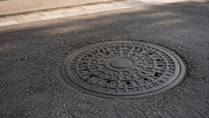 Warum sind Kanaldeckel rund? Runder Kanaldeckel auf einer Asphaltstraße aus schräger Perspektive