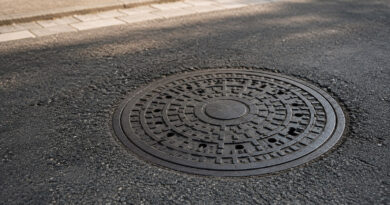 Warum sind Kanaldeckel rund? Runder Kanaldeckel auf einer Asphaltstraße aus schräger Perspektive